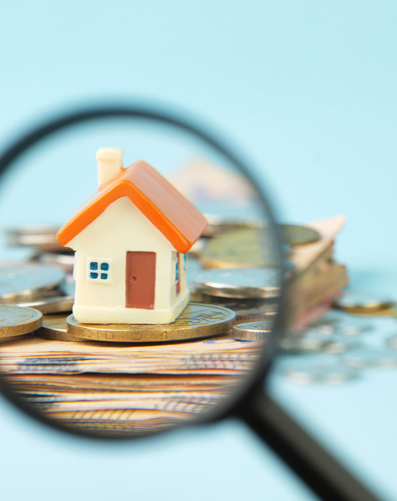 Lupa analisando uma casa miniatura sobre moedas, imagem para o artigo "Laudo de avaliação de imóvel: engenheiro ou corretor? A resposta definitiva!".