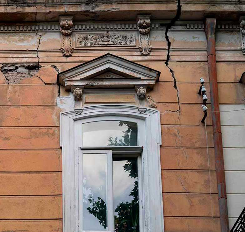 fachada de imóvel antigo com grandes rachaduras estruturais ilustrando a necessidade de uma vistoria cautelar de vizinhança nível 3 detalhada.