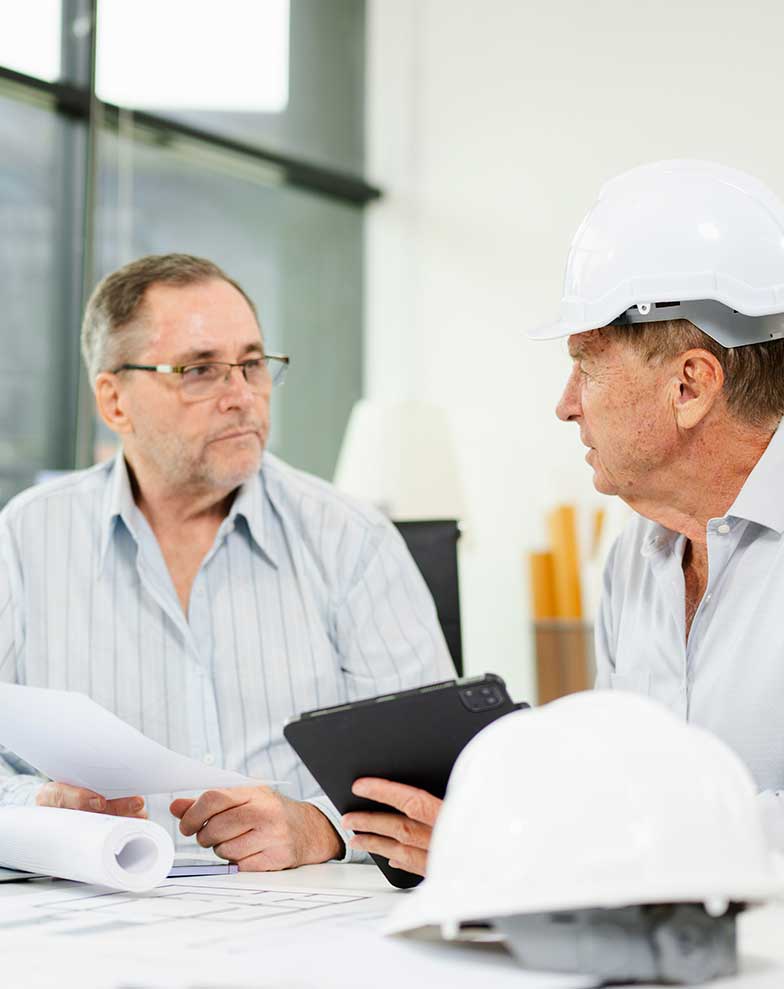 engenheiro civil de capacete branco e gestor jurídico ou advogado analisando plantas e documentos em escritório para definir estratégia de produção antecipada de prova.