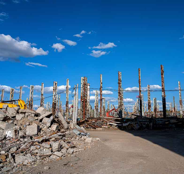 canteiro de obras de infraestrutura paralisado com montanha de escombros de concreto e pilares de aco expostos sob ceu azul ilustrando o risco de maquinario ocioso por falhas nas desapropriacões em ppps
